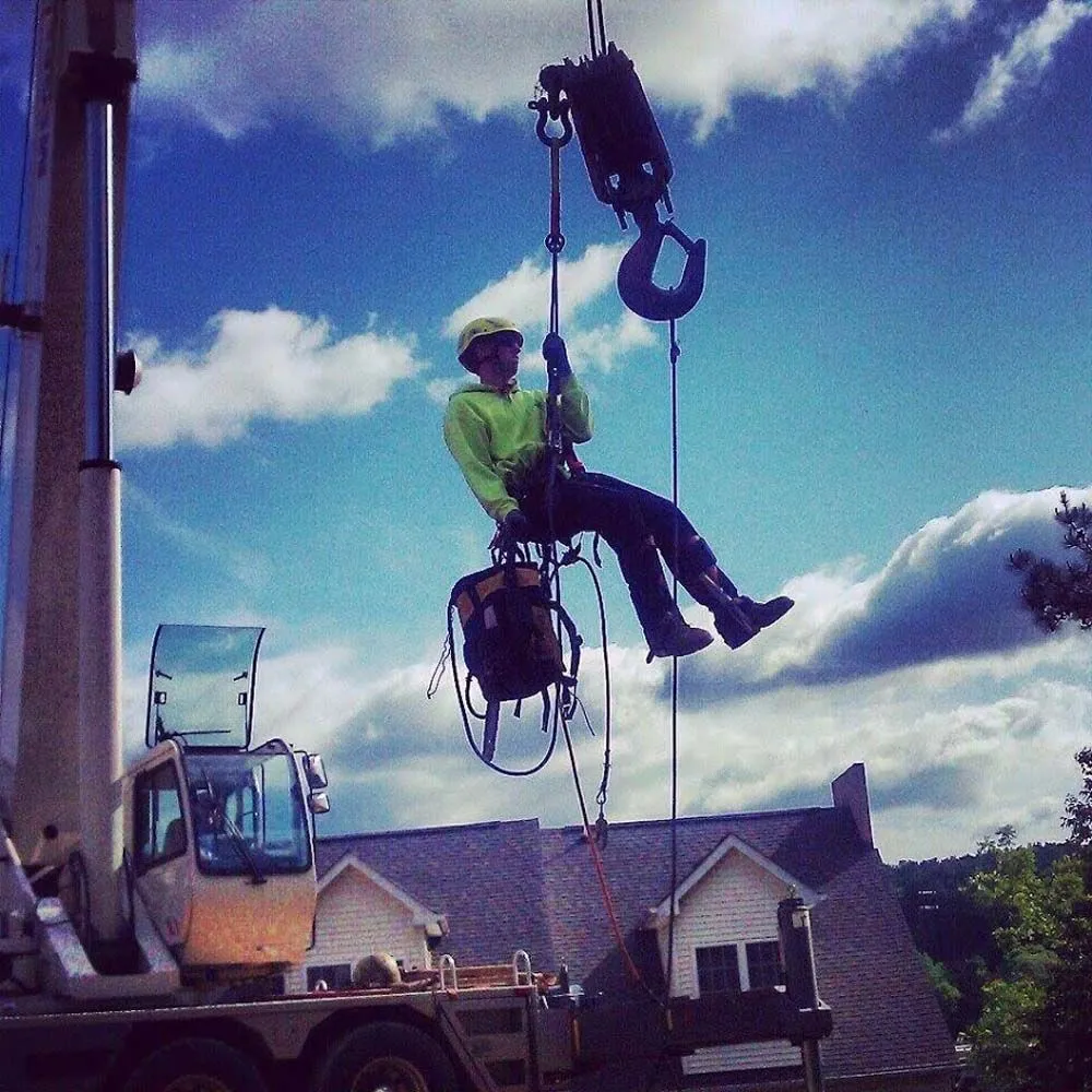 Arborist in safety gear suspended from crane hook during operation
